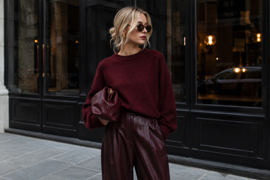Mulher loira usando look sofisticado em tom vermelho cereja, com bolsa de couro e composição elegante inspirada nas principais tendências de looks de outono; produção fashion em cenário urbano.